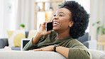 Happy African woman talking on the phone while relaxing on her cozy sofa at home. Cheerful black female laughing while having a pleasant and funny conversation with a friend on her mobile