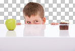 A young boy tempted by the sight of a chocolate cake and an apple on a table making an unhealthy decision, choosing sweets or unhealthy snacks such as a cupcake isolated on a PNG background.