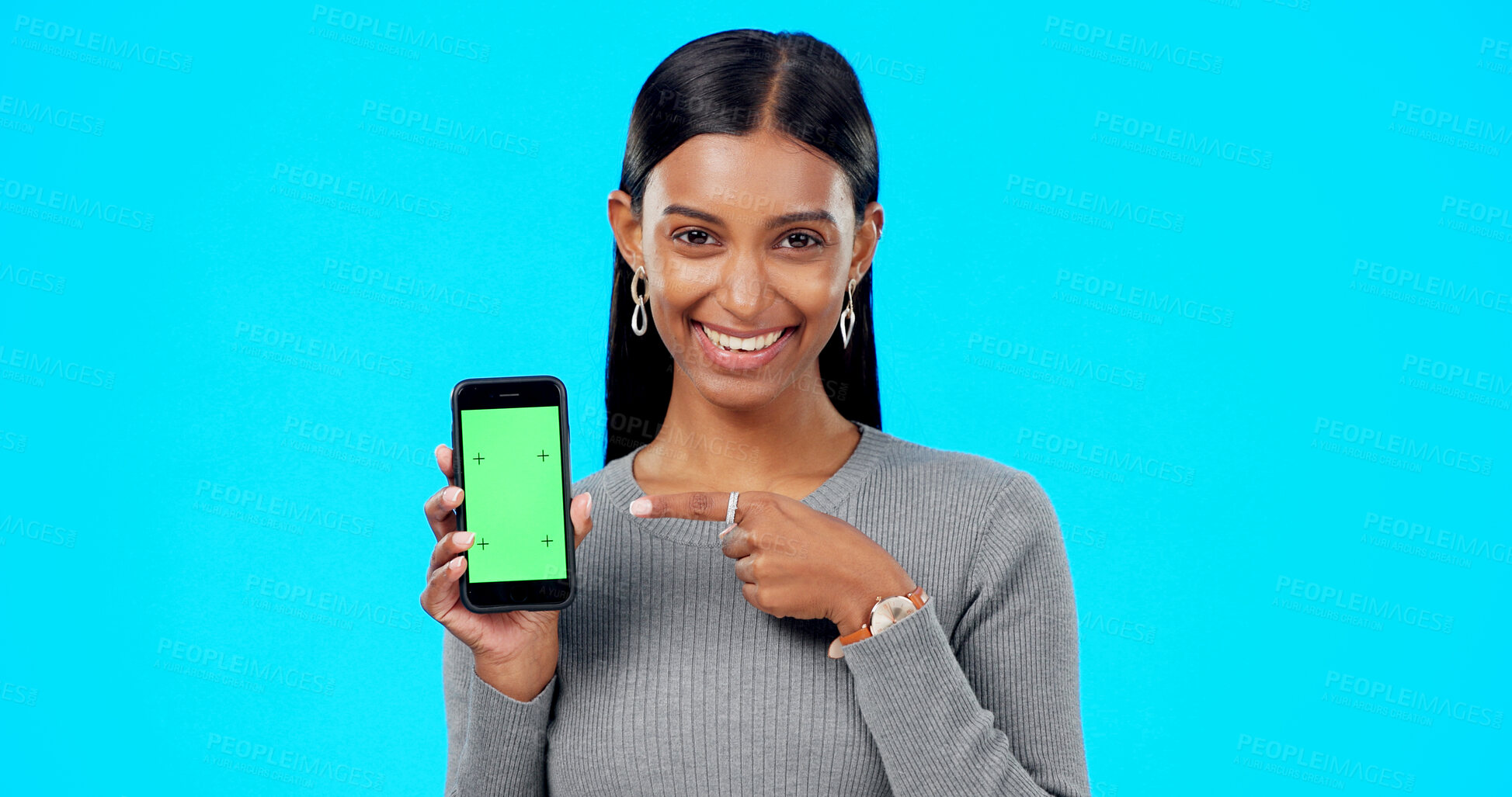 Buy stock photo Portrait, woman and advertising green screen of phone, space and sign up offer in studio on blue background. Happy indian model pointing to mobile tracking markers for news, mockup promotion and deal