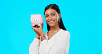 Piggy bank, happy face and Indian woman with a smile from savings, investment and finance. Isolated, blue background and portrait of a young female with happiness from cash saving and safe budget