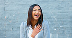 Cheerful woman laughing and giggling about something funny while standing outside against a grey wall with copy space. Happy businesswoman having fun and expressing positivity and a playful attitude