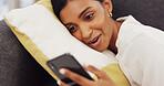 Girl on sofa, smiling and typing on a phone in living room. Social media, technology and communication, a happy young woman lying on a couch and chatting to friends online or watching a funny video.