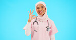 Face, nurse and Muslim woman with ok sign in studio isolated on blue background mockup. Smile, portrait and happy medical professional or Islamic person with okay emoji, hand gesture, like or success
