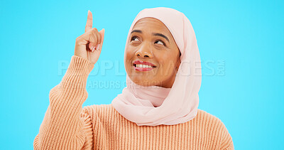 Buy stock photo Muslim woman, happy and pointing up to idea on mockup space for advertising or promotion. Arabic female person with smile and hijab for islamic announcement or sale choice on blue background studio