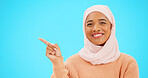 Woman, pointing finger and space for happy muslim announcement with hand for mockup. Islamic female with hijab and face with smile for sale, promotion or product placement on studio blue background