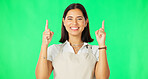 Woman, smile and portrait on green screen while pointing finger up at mockup space with apron. Female model happy about advertising business or promotion or choice in air on a studio background