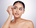 Face, woman with eye pencil and makeup against a studio background. Cosmetics or dermatology, skincare or beauty treatment  and female person shaping her eyebrows with a brush against backdrop