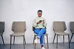 Black woman, phone and sitting on a chair in a waiting room with internet connection for social media. African female person in line for recruitment interview with a smartphone for communication app