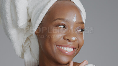 Buy stock photo Face, beauty and cream with a happy black woman in studio on a gray background for natural wellness. Skincare, smile and lotion with a happy young model closeup to apply treatment to her skin