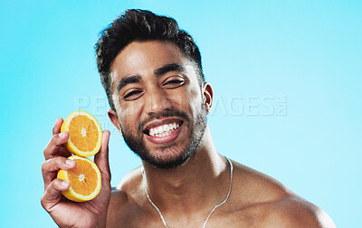 Happy, orange and face of man in studio for skincare, wellness and citrus treatment on blue background. Fruit, facial and portrait of indian male model excited for organic vitamin c skin cosmetics