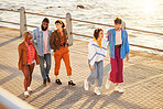 Friends, sea and diversity with people walking on the promenade together during summer from above. Happy, smile and ocean with a man and woman friend group bonding during a walk outside by the beach