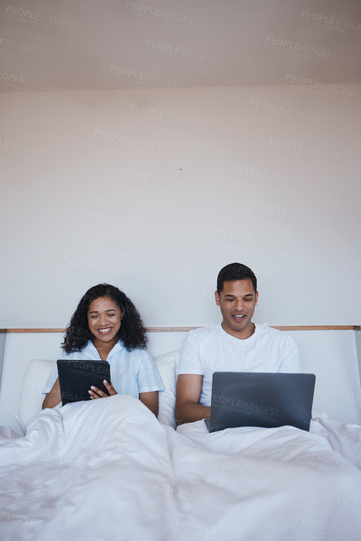 Buy stock photo Technology, relax and couple in bed networking on social media or the internet together at home. Happy, smile and young man and woman browsing on a digital tablet and laptop in bedroom in the morning