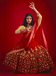 Portrait, dance and Indian woman with fashion, traditional dress and celebration against a red studio background. Face, female person or model with cultural clothes, jewellery and dancing with beauty