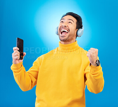 Buy stock photo Celebration, man with smartphone and headphones against blue background listening to radio. Music or podcast, success or achievement and male person with cellphone happy for playlist or streaming