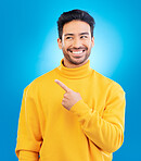 Man, point and thinking with smile in studio for ideas, fashion and promotion with choice by blue background. Young Indian guy, happy student and finger for decision, icon and opinion with show