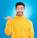 Portrait, man and pointing to advertising space in studio, blue background and mockup of deal, promotion or news.  Happy asian, male model and presentation of announcement, information or opportunity