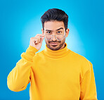 Cool, fashion and portrait of a man with glasses, confidence and winter aesthetic. Sexy style, trendy and a fancy Asian model with fashionable eyewear isolated on a blue background in a studio