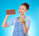 Apple, chocolate and woman for healthy food choice or offer isolated on studio, blue background for food, sugar and diet. Dessert, green fruit and happy young person for detox or lose weight decision