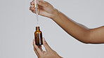 Closeup, hands and pipette for skincare, cosmetics and dermatology against a grey studio background. Zoom, hand and bottle with serum, collagen and oil for treatment, grooming and product for beauty