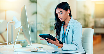 Businesswoman typing out financial reports while working on a tablet in her office. Female accountant managing finances and doing bookkeeping using software to compile data and writing notes