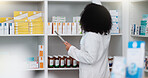Young and focused pharmacist use her tablet to do stock taking in a modern pharmacy drugstore. Multiethnic female health professional worker or medication expert in a chemist using a digital gadget