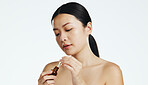 Asian woman, dropper and keratin on face for beauty, skincare or cosmetics against white studio background. Happy female model applying oil drop to skin for hydration, moisturizer or facial treatment