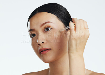 Asian woman, dropper and keratin on face for beauty, skincare or cosmetics against white studio background. Happy female model applying oil drop to skin for hydration, moisturizer or facial treatment