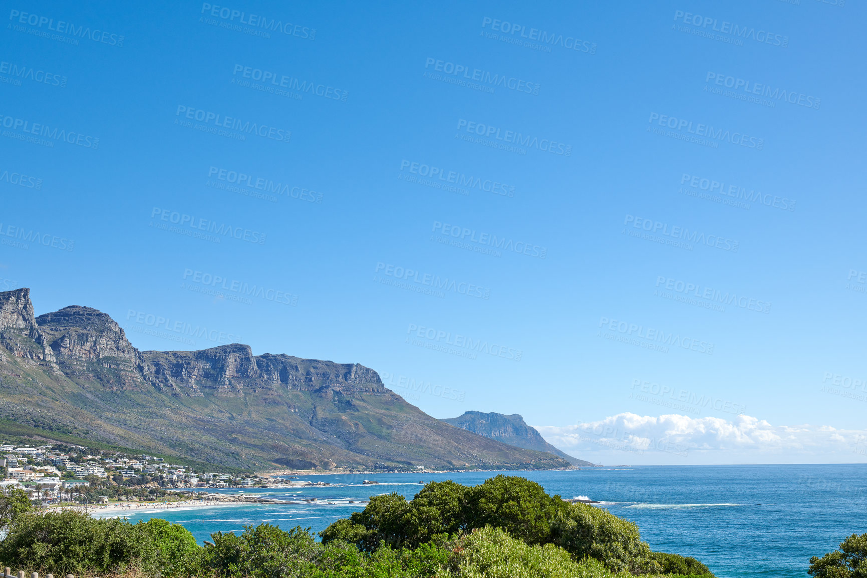 Buy stock photo Costal city surrounded by nature with an iconic landmark in the background in urban Cape Town. Scenic view of mountain with vibrant green plants near a calm ocean and a blue sky day with copy space. 