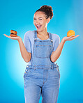 Portrait, excited and woman with donut, orange and choice in studio isolated on blue background. Happy, fruit or person with doughnut, fast food or comparison for healthy diet, nutrition or wellness
