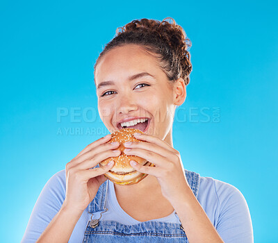 Buy stock photo Burger, smile and woman eating fast food and happy with lunch meal with a smile isolated in a studio blue background. Breakfast, craving and portrait of young female person enjoy snack or sandwich