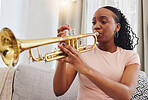Music, sofa and woman in home with trumpet, sound and band practice for orchestra concert in living room. Art, creativity and jazz culture, African musician on couch in performance and musical talent