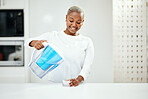 Woman, pitcher and glass of filter water to refresh in liquid purification treatment at home. Happy black female person pouring healthy aqua beverage for nutrition, drink or filtration jug in kitchen