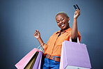 Bags, excited and black woman with a credit card, shopping and boutique items on a grey studio background. Female person, shopper or model with celebration, payment and smile with sales and luxury