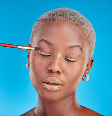 Buy stock photo Face, makeup and eyeshadow with a black woman on a blue background in studio to apply a beauty product. Cosmetics, gold color on a brush and a young female model eyes closed for style or glamour