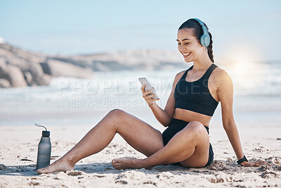 Buy stock photo Fitness, break and happy woman relax at beach with phone, music and headphones after training. Exercise, resting and lady health influencer posting to social media, blog or podcast after ocean run