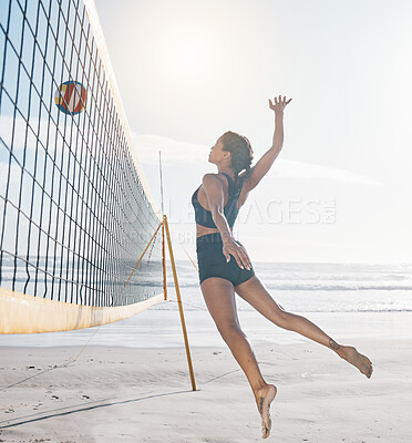 Woman, jump and volleyball on beach by net in serious sports match, game or competition in nature. Fit, active and sporty female person jumping or reaching for ball in volley for spike by the ocean