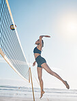 Woman, jump and volleyball player on beach by net in serious sports match, game or competition. Fit, active and sporty female person jumping or reaching for ball in volley or spike by the ocean coast