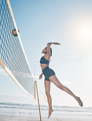 Woman, jump and volleyball player on beach by net in serious sports match, game or competition. Fit, active and sporty female person jumping or reaching for ball in volley or spike by the ocean coast