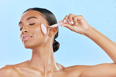 Buy stock photo Facial massage, woman and roller, natural beauty and skincare, cosmetics and tools isolated on blue background. Rose quartz, crystal and skin glow, Indian female model with dermatology and antiaging