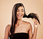 Smile, beauty and a woman brushing her hair in studio on a cream background for natural or luxury style. Haircare, face and shampoo with a happy young indian female model at the salon or hairdresser