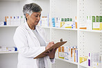 Pharmacist, medicine and a woman writing on a clipboard in a pharmacy for inventory or checklist. Mature female employee check shelf for management in healthcare, pharmaceutical and medical industry
