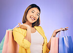 Asian woman, portrait and shopping bag with retail and fashion, commercial and sale on purple background. Discount at boutique, happy female customer and market with store promotion in studio