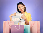 Shopping bag, portrait and woman for clothes sale, discount or giveaway promotion on studio, purple background. Happy young model, customer or asian person for fashion choice, retail or unboxing gift