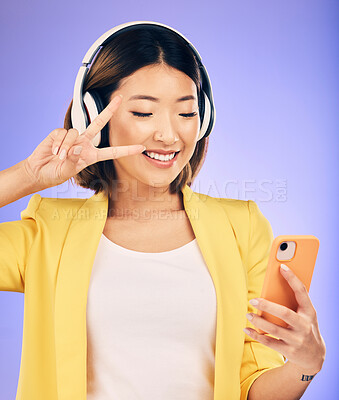 Buy stock photo Peace sign, selfie and happy Asian woman in studio smile for social media, online post or mobile app. Headphones, music and female person with emoji on smartphone listen to audio on purple background