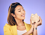 Piggy bank, finance and woman thinking of savings, investment and happy for money growth goals. Young asian person for financial management, money safe or banking security on studio purple background