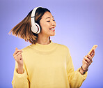 Headphones, music and Asian woman dance with phone in studio for streaming, subscription and radio. Happy female person on smartphone listening to audio, song and track on purple background to relax