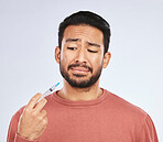 Vaccine, fear and face of asian man in studio with needle, phobia or covid scare on grey background. Corona, compliance and male person afraid of vaccination, medicine or prescription diabetic shot