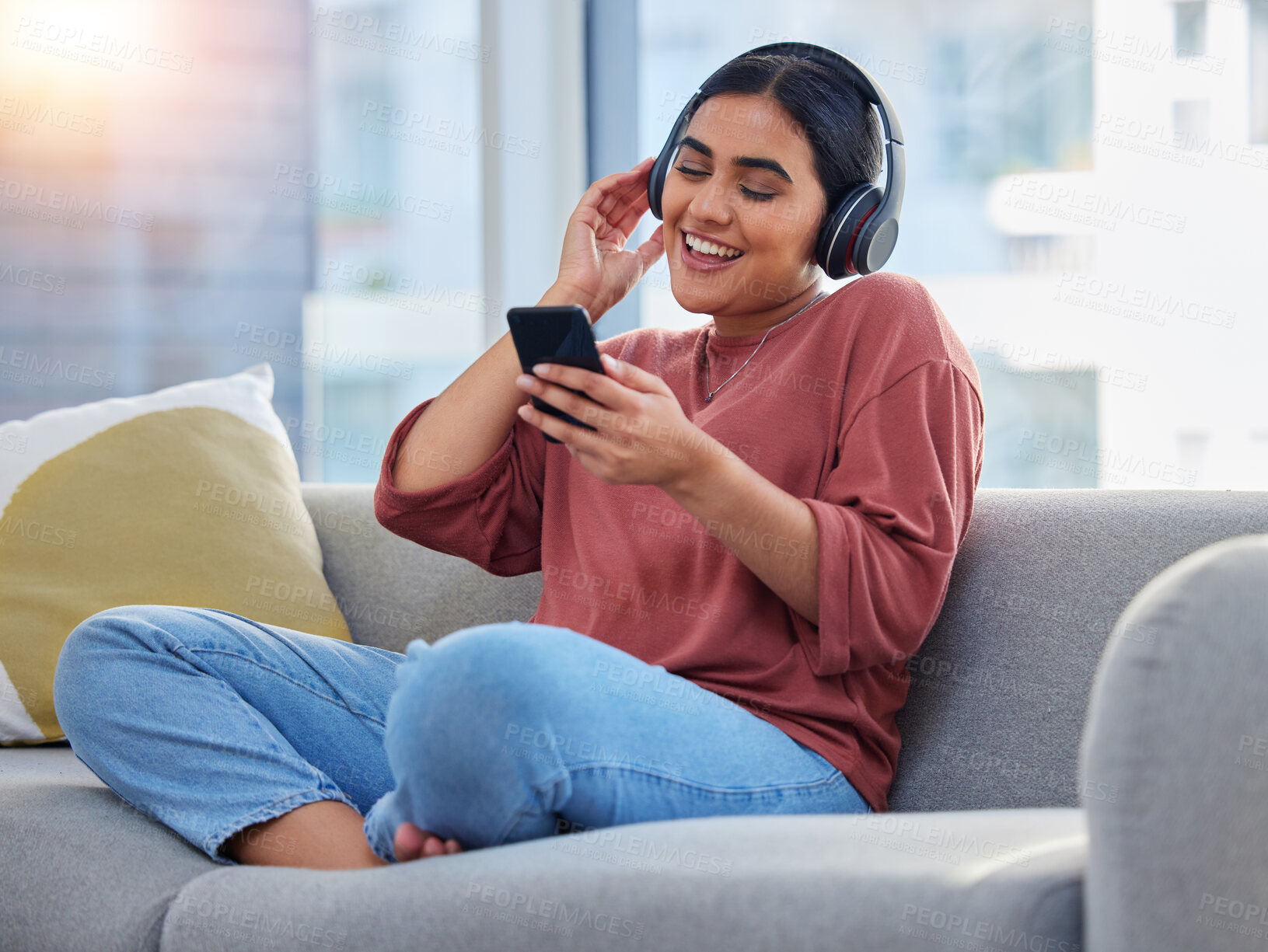 Buy stock photo Relax, music and phone with woman on sofa and dance for streaming, social media and audio. Happy, technology and radio with person listening to headphones in living room at home for energy and sound