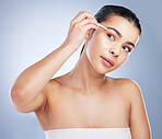 Young woman tweezing her eyebrows in a studio for grooming or hair removal face routine. Skincare, beauty and female model doing a facial epilation treatment with tweezers isolated by gray background