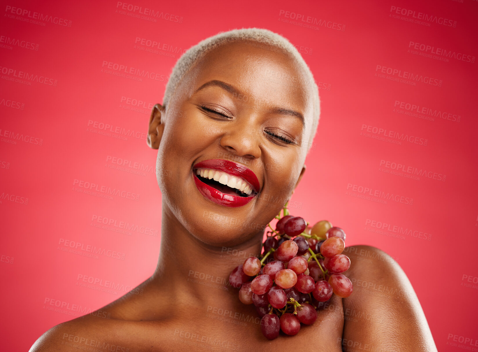 Buy stock photo Beauty, smile and grapes with a model black woman in studio on a red background for health or nutrition. Skincare, happy and fruit with a young female person posing for wellness, diet or detox